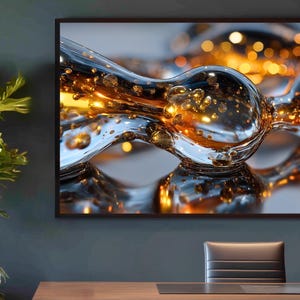 May include: Abstract art print showing a close-up of a glass sculpture with a liquid appearance. The artwork has a reflective surface with golden orbs and a dark frame. The print is displayed on a dark grey wall above a wooden desk.