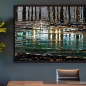 Op de afbeelding: Een abstract landschapsschilderij in een donkerhouten lijst. Het kunstwerk toont een bosscène met lange, verticale bomen die weerspiegeld worden in een waterpartij. Het kleurenpalet omvat tinten groen, bruin en goud.