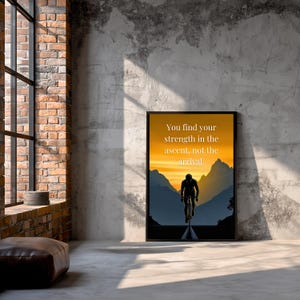 May include: A framed print with a cyclist silhouette set against a sunset. The artwork displays the text: "You find your strength in the ascent, not the arrival." The colour scheme includes orange, yellow, blue, and black.
