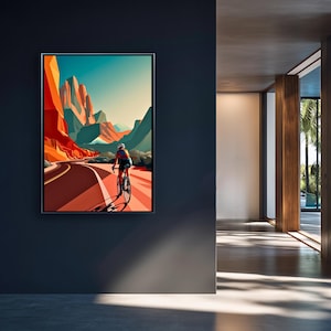 May include: A framed art print depicts a cyclist riding on a winding road through a desert landscape. The artwork features vibrant colors, with red and orange rock formations, a blue sky, and a cyclist in motion. The print is displayed on a dark blue wall.