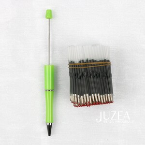 May include: A lime green pen with a silver accent and a black tip is displayed next to a bundle of black ink pen refills secured with a brown rubber band. The pen has a long, thin silver rod extending from the top.