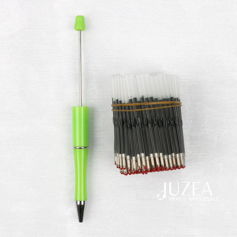 May include: A lime green pen with a silver accent and a black tip is displayed next to a bundle of black ink pen refills secured with a brown rubber band. The pen has a long, thin silver rod extending from the top.