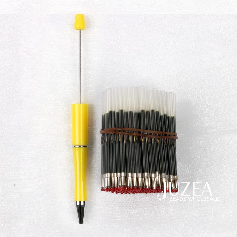 May include: A yellow pen with a silver tip and a bundle of black ink refills bound with a brown rubber band. The pen has a yellow cap and a silver metal shaft. The ink refills have red tips.