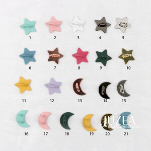 Puede incluir: Una colecci&oacute;n de botones met&aacute;licos en forma de estrella y media luna en varios colores, incluyendo azul, rosa, blanco y dorado. Los botones est&aacute;n dispuestos sobre una superficie blanca, cada uno numerado.