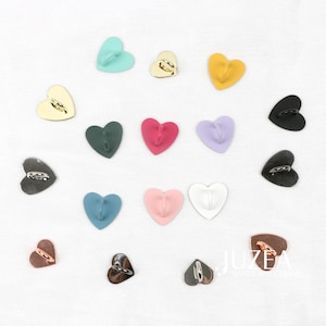 May include: A collection of heart-shaped wall hooks in diverse colours, such as gold, black, pink, and blue. Each hook features a small loop for hanging. The hooks are displayed on a white surface.