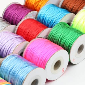 May include: A selection of colourful cord spools. The spools are arranged in rows, displaying a range of colours such as purple, orange, blue, red, green, and pink. The cord appears to be made of a smooth, shiny material.
