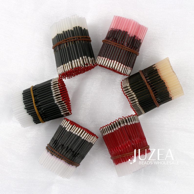 May include: Overhead shot of six bundles of beads, each secured with a brown rubber band. The beads are black, red, and white, with silver-colored tips. The image is well-lit, showcasing the variety of colors and textures.
