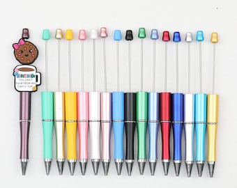 May include: A collection of fifteen metal pens with colorful barrels and matching toppers. One pen features a decorative charm of a cookie and a coffee mug with the text "REMINDER: YOU CAN'T POUR FROM AN EMPTY CUP." The pens have silver tips and clips.