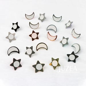 Puede incluir: Un surtido de hallazgos de joyer&iacute;a en forma de estrella y media luna. Los hallazgos son de varios colores, incluyendo negro, gris y oro rosa, con un centro circular blanco. La imagen est&aacute; sobre un fondo blanco.