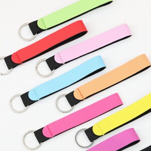 May include: A collection of colorful keychains with a loop strap and a metal ring. The keychains come in various colors, including green, red, pink, blue, orange, and yellow. The straps are attached to a black fabric.