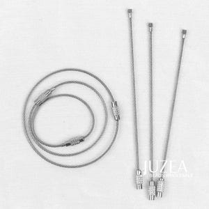 May include: An assortment of silver-toned jewellery cords and wires. Some are coiled, while others are straight with decorative ends. The image includes the text "JUZEA BEADS WHOLESALE".