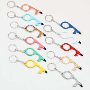 Op de afbeelding: Een verzameling sleutelhangers in diverse kleuren, waaronder roségoud, blauw, iriserend, roze, groen, geel, wit, rood, goud en zilver. Elke sleutelhanger heeft een flesopener en een stylus tip.