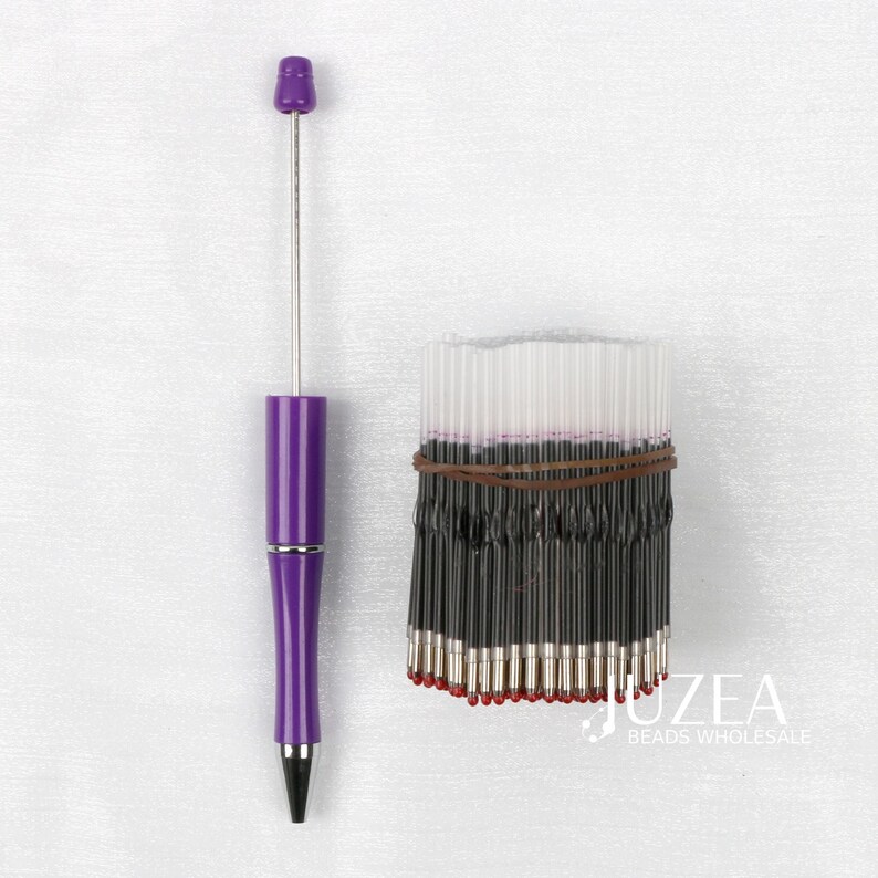 May include: A purple pen with a silver tip and a bundle of black ink refills with red tips, held together by a brown rubber band. The pen has a matching purple cap.