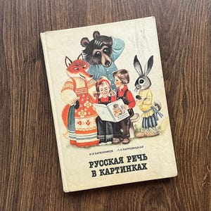 Pode incluir: Um livro de capa dura intitulado "РУССКАЯ РЕЧЬ В КАРТИНКАХ" por И В БАРАННИКОВ e Л А ВАРКОВИЦКАЯ. A capa apresenta uma ilustração colorida de uma raposa, um urso, um coelho e duas crianças lendo um livro juntas em um fundo de cor creme.
