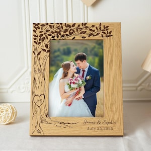 Peut inclure: Un cadre photo en bois avec une photo de mariage. Le cadre présente un motif d'arbre sculpté. La photo montre une mariée et un marié. Les noms "James & Sophia" et la date "July 25, 2025" sont imprimés sur le cadre.