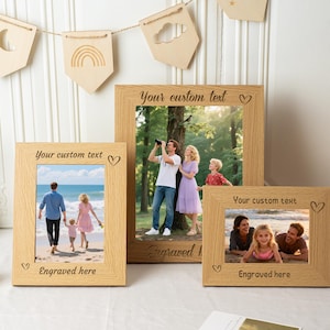 May include: Three wooden photo frames in different sizes, with a light wood grain. Each frame holds a family photograph and features the text "Your custom text" and "Engraved here". A decorative banner with wooden cutouts hangs above.