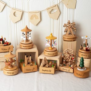 Peut inclure: Plusieurs boîtes à musique en bois avec des thèmes variés, comme un carrousel, une grande roue et un château. Chaque boîte est gravée d'un nom. Les boîtes sont exposées sur de petits socles en bois, avec une bannière de formes en bois en arrière-plan.