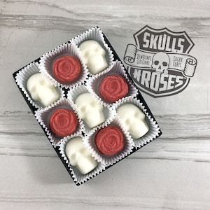 Tile background with open box of skull shaped sugar cubes & red rose shaped sugar cubes, each sugar cube sits in a white candy cup in a grid, Rubber stamp logo over image reads: Skulls N Roses, DemBones Original, Sugar Cubes