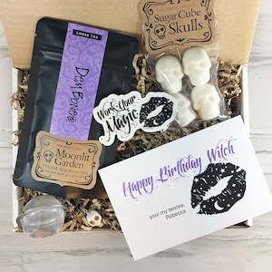 May include: A gift box filled with Halloween-themed items, including a bag of loose leaf tea labeled "Dem Bones", a card that says "Happy Birthday Witch", sugar cube skulls, and a tea infuser.