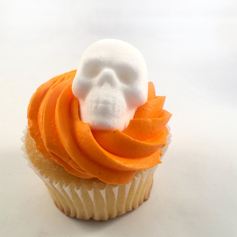 DemBones skull sugar cube sitting on orange frosting off store bought cupcake, white and orange halloween colors