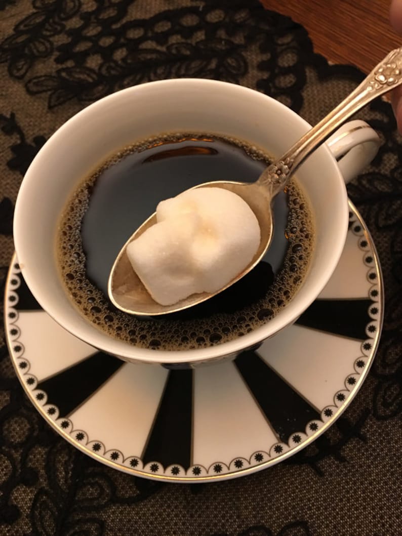 Gothic tea cup and saucer with black and white stripes, Cup is full of black coffee and sugar cube in silver spoon is above it frozen in time the moment before it is stirred into the coffee,