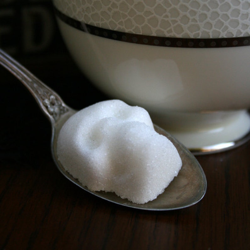 Close up of skull sugar cube sitting on vintage silver spoon next to white tea cup on dark wood table