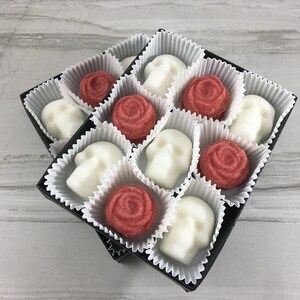 Two stacked boxes of skull shaped sugar cubes and red rose shaped sugar cubes, each sugar cube sits in a white candy cup in a grid, tile background