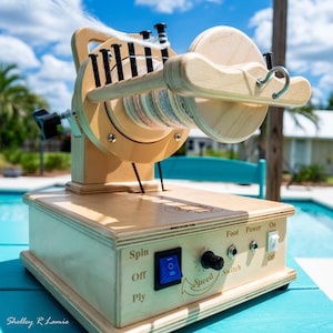 May include: A wooden spinning wheel with a light finish. The wheel has a large spool of colorful yarn and a control panel with a speed dial and power switch. The wheel is sitting on a blue surface.