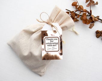 May include: A beige linen gift bag tied with twine, featuring a tag with a brown and white cowhide pattern. The tag reads "Thank you for celebrating with me! Love, Olivia" in a brown font.