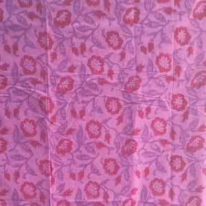 Può includere: Un tessuto rosa con un motivo floreale. Il design presenta fiori rossi e foglie e viti viola su sfondo rosa. Un bordo decorativo con un motivo floreale si trova nella parte inferiore.