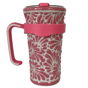 May include: A tall, insulated travel mug with a decorative floral pattern in shades of pink and white. The mug features a pink handle, a pink silicone band, and a pink lid. The mug is designed to keep beverages hot or cold.