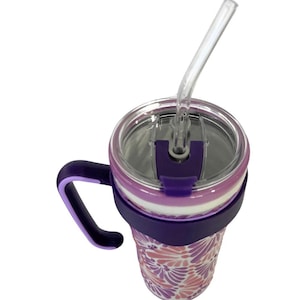 May include: A purple and pink floral patterned tumbler with a clear straw. The tumbler has a purple handle and a lid with a clear plastic straw. The design features a floral pattern in shades of pink and purple.