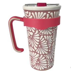 Puede incluir: Un termo de viaje rosa y blanco con estampado floral, con asa y tapa. El termo tiene una banda y un asa de silicona rosa. El estampado floral es blanco y en relieve sobre el fondo rosa. La tapa es transparente con un deslizador rosa.