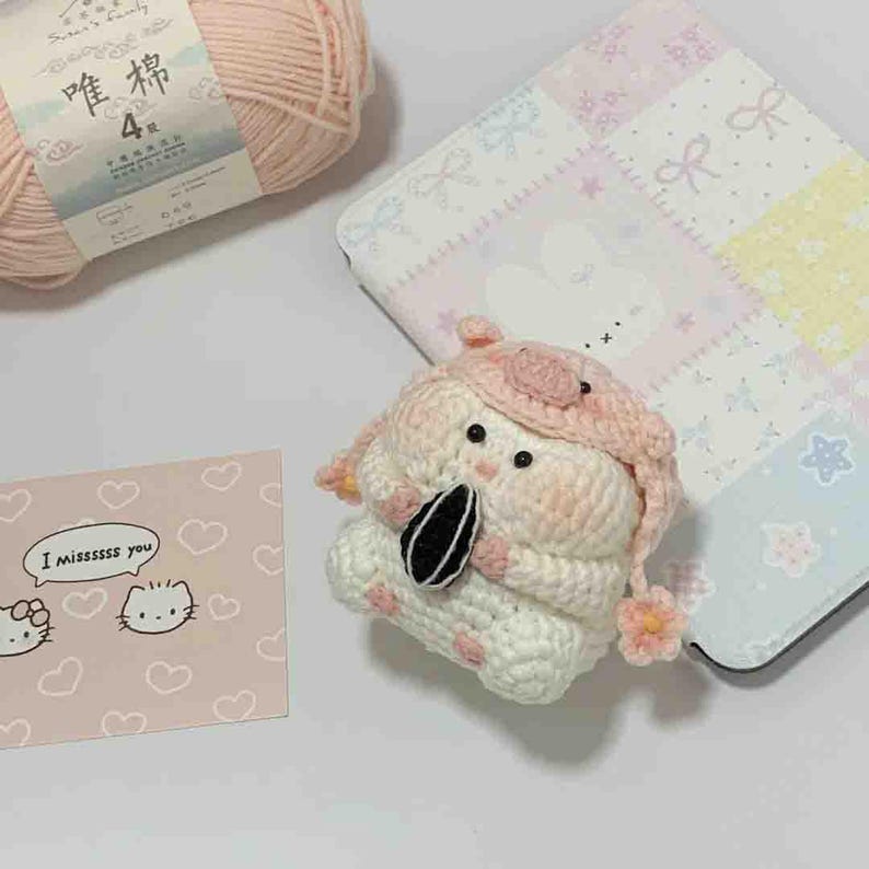 Puede incluir: Una mu&ntilde;eca de conejito de ganchillo hecha a mano en blanco y rosa, con un sombrero rosa con una flor. La mu&ntilde;eca sostiene una semilla de girasol en blanco y negro. Una tarjeta rosa con el texto "I missssss you" y una madeja de hilo rosa tambi&eacute;n est&aacute;n en la imagen.