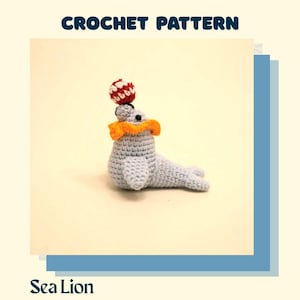 May include: A crocheted sea lion toy in light blue, with an orange collar and a red and white ball balanced on its head. The words "CROCHET PATTERN" and "Sea Lion" are displayed in the image.