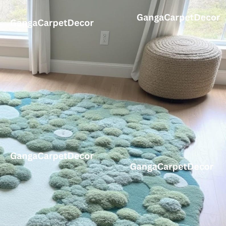 Puede incluir: Una alfombra inusual, de forma irregular, con un dise&ntilde;o texturizado en tres dimensiones. La alfombra presenta una mezcla de tonos verdes claros y oscuros, y azules, que recuerdan a un paisaje. Un otom&aacute;n redondo y tejido est&aacute; cerca. El texto "GangaCarpetDecor" es visible.