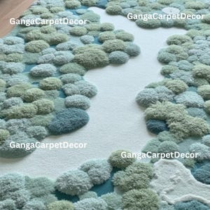 Puede incluir: Una alfombra texturizada con dise&ntilde;o de paisaje. La alfombra presenta formas redondeadas y afelpadas en tonos verdes, azules y blancos, que se asemejan a una escena de bosque o paisaje. El fondo es de color claro y neutro, creando un contraste con los elementos texturizados.