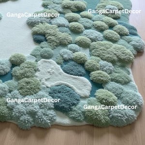Puede incluir: Una alfombra tupida con dise&ntilde;o de paisaje. La alfombra presenta una mezcla de texturas y colores, incluyendo tonos de verde, azul y blanco, creando un efecto tridimensional. El texto "GangaCarpetDecor" es visible en varios lugares.