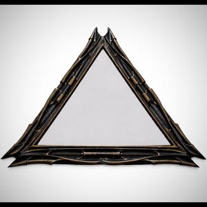 May include: A triangular mirror with a dark bronze frame. The frame has an intricate, textured design with a geometric pattern. The mirror is set against a white background.