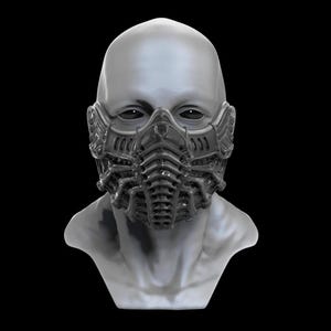 May include: A futuristic, dark gray mask with intricate, mechanical detailing. The mask covers the lower face and nose, featuring a segmented design with multiple layers and a textured surface. The mask is set against a black background.
