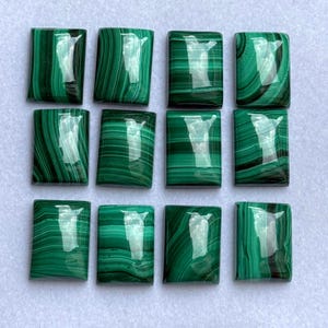 Puede incluir: Doce piedras preciosas rectangulares de malaquita con un acabado pulido y brillante. Las piedras muestran un color verde oscuro intenso con patrones arremolinados y vetas verdes más claras. Las piedras están dispuestas en forma de cuadrícula.