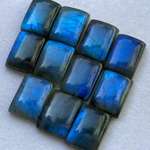 Pode incluir: Uma coleção de pedras preciosas de labradorita retangulares. As pedras exibem uma gama de azuis e cinzas, com flashes iridescentes. As superfícies polidas refletem a luz, mostrando os padrões naturais. Adequadas para a criação de joias.