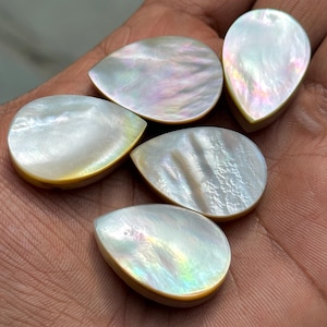 Könnte beinhalten: Fünf tropfenförmige Cabochons aus schillerndem Perlmutt. Jeder Cabochon hat einen perlmuttartigen Glanz mit Andeutungen von Rosa, Grün und Gelb. Die Ränder sind warm goldfarben. Ideal für Schmuckherstellung oder andere Bastelprojekte.