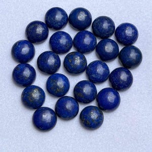Könnte beinhalten: Eine Ansammlung runder, polierter Lapislazuli-Edelsteine. Die tiefblauen Steine haben goldene Flecken und sind kreisförmig angeordnet. Diese Edelsteine eignen sich für die Schmuckherstellung oder zum Sammeln.