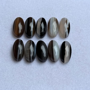 May include: Ten oval gemstones with a polished finish. The stones display a banded pattern of brown, black, and white, with variations in colour intensity. The gemstones are arranged in two rows of five, showcasing their natural beauty and unique striations.