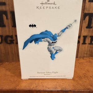 以下が含まれることがあります： ダイナミックなポーズのバットマンをフィーチャーした、Hallmark Keepsakeのクリスマスツリーオーナメント。フィギュアは主にグレーで、青いマントとブーツが付いています。パッケージにはバットマンのロゴと「Batman Takes Flight」の文字が含まれています。