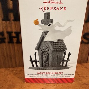 Può includere: Un ornamento per albero di Natale Hallmark Keepsake con Zero da The Nightmare Before Christmas di Tim Burton. L'ornamento raffigura Zero con un naso di zucca, una croce e una casa con la parola "ZERO".