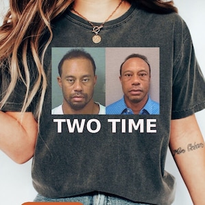 May include: Dark gray t-shirt featuring two mugshot images of a man, with the text "TWO TIME" in white block letters. The word "Pepper" is printed on an orange oval at the bottom of the shirt.