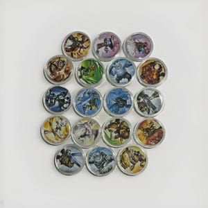 May include: A collection of round, silver-rimmed buttons featuring colourful illustrations of fantasy characters. The buttons are arranged on a white surface, displaying a variety of designs and colours.