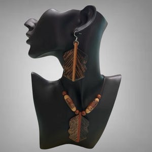 May include: A wooden necklace and earrings set with brown and tan leaf-shaped pendants. The necklace has brown and tan wooden beads.